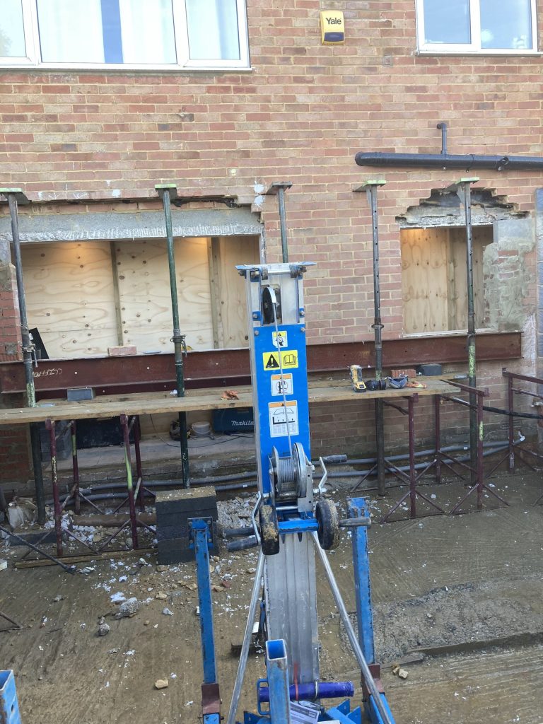 Steel beams on temporary props across the back of a brick house during a structural alteration